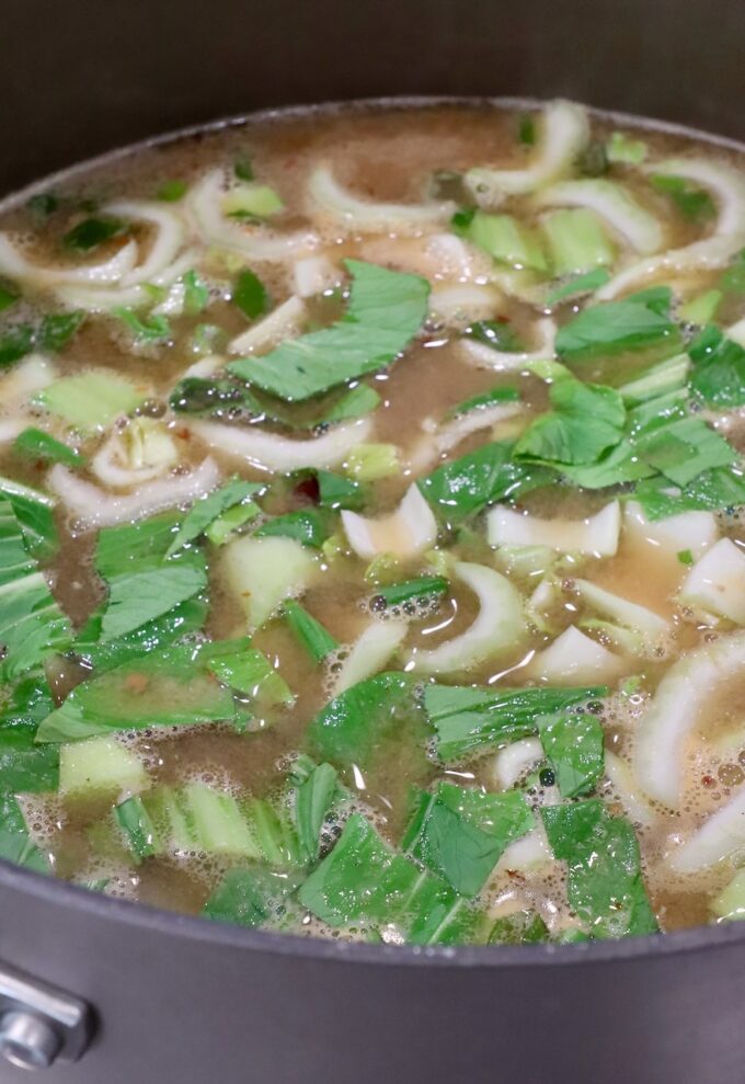 baby bok choy chopped up in a pot of broth on the stove