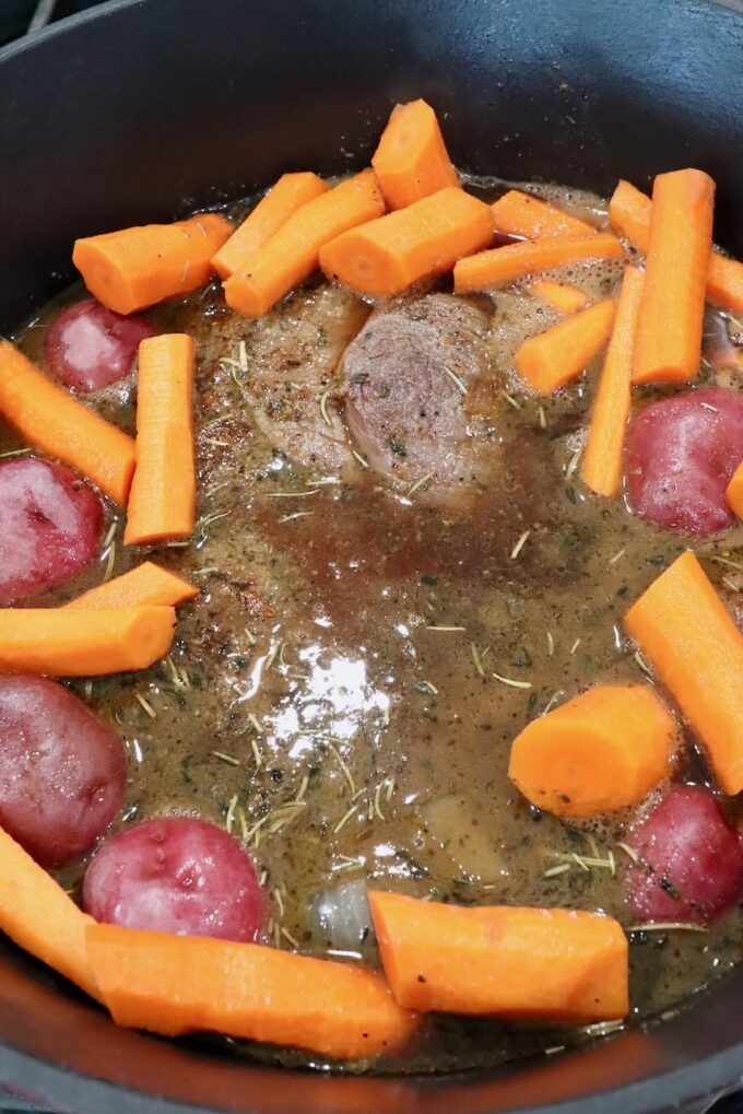 chuck roast in liquid in a dutch oven with carrots and potatoes