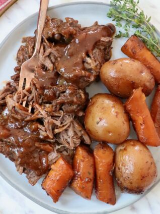 pot roast with gravy on a plate with a fork, potatoes and carrots