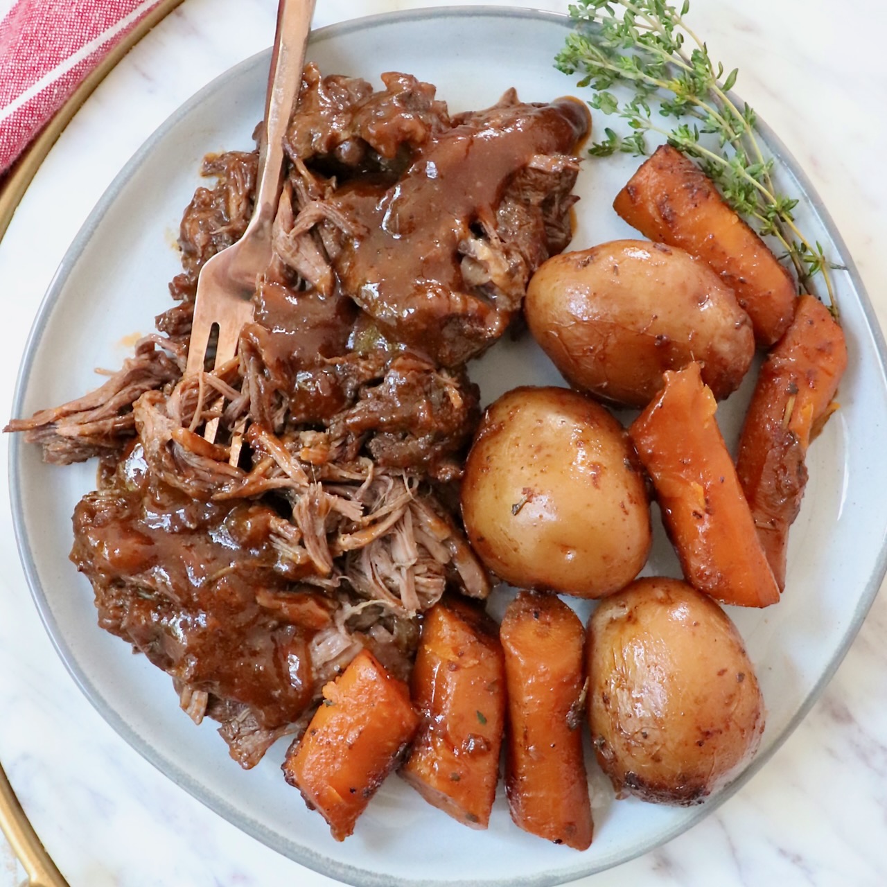 pot roast with gravy on a plate with a fork, potatoes and carrots