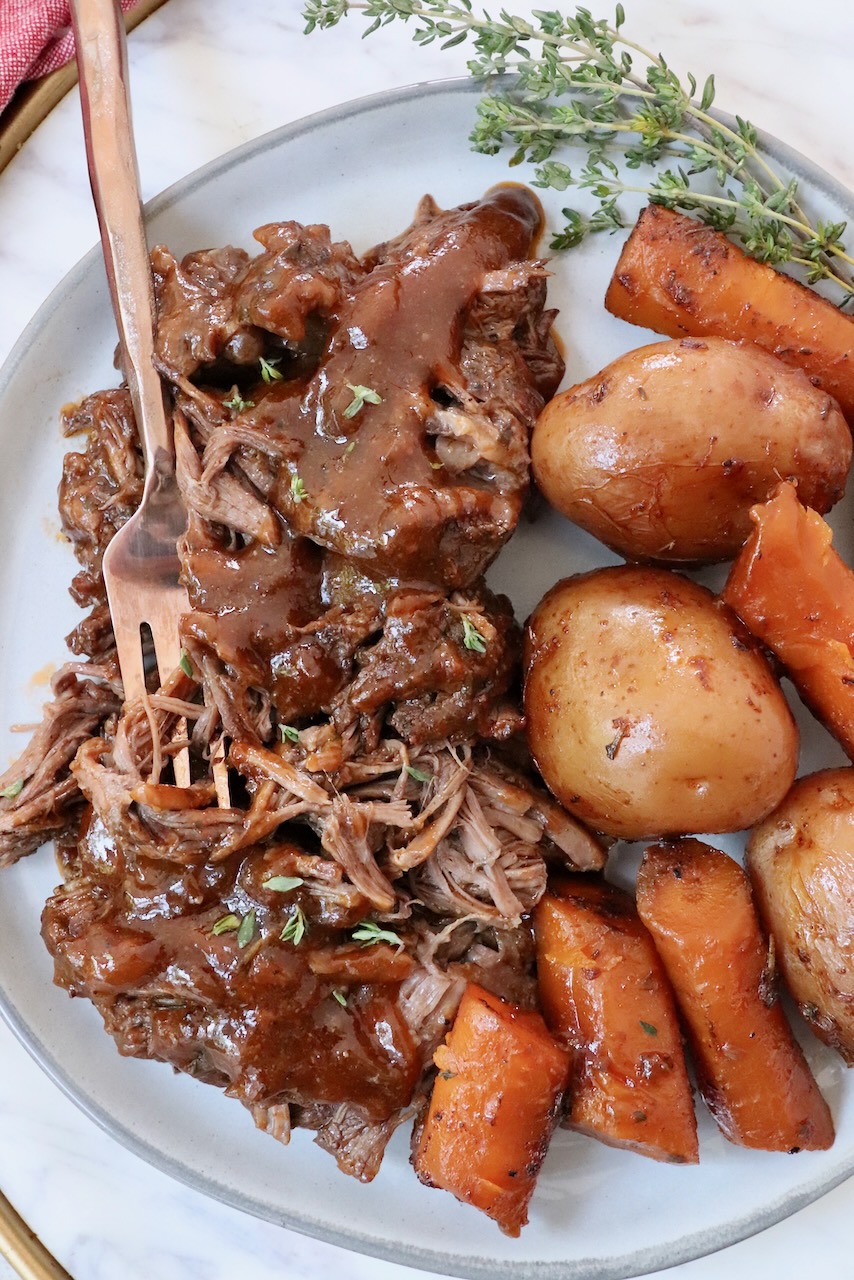 shredded pot roast on plate with gravy, potatoes and carrots