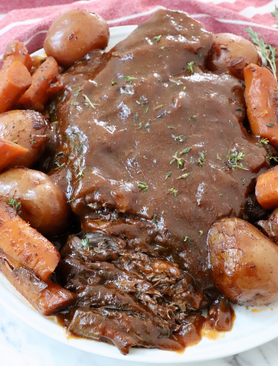 pot roast on plate, topped with gravy, surrounded by roasted potatoes and carrots