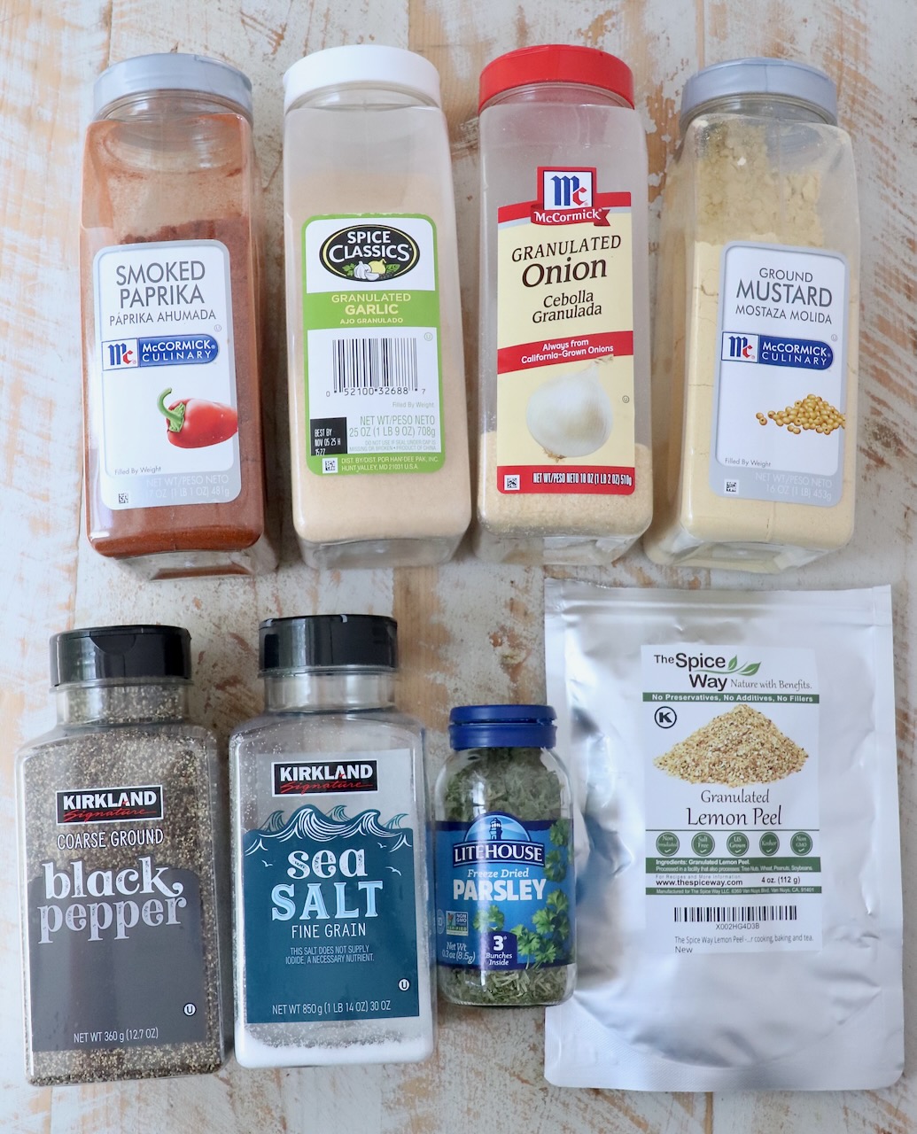 herbs and spices in plastic containers and jars on a white wood board