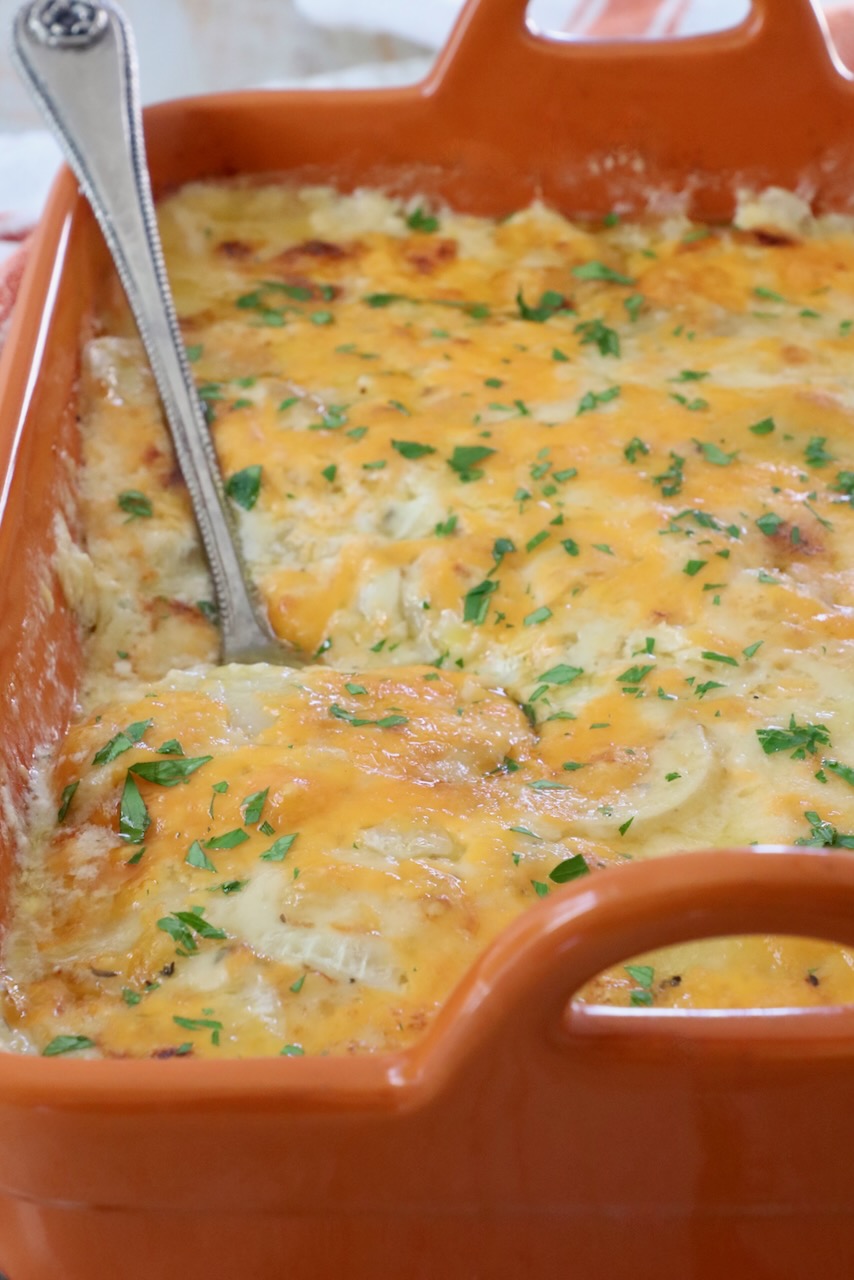 au gratin potatoes in an orange casserole dish with a serving spoon