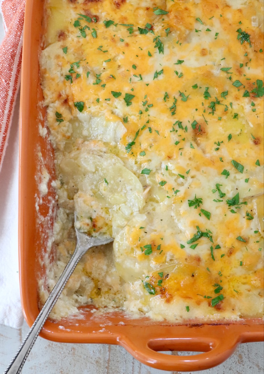 au gratin potatoes in an orange baking dish with a serving spoon