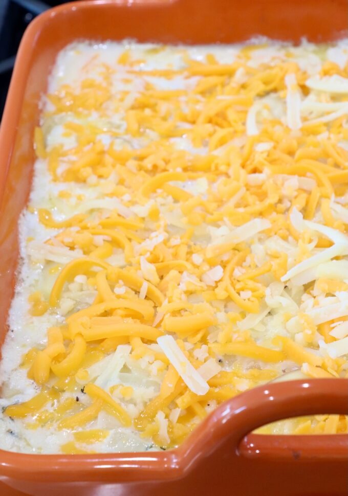 layered creamy potatoes in a baking dish topped with shredded cheese