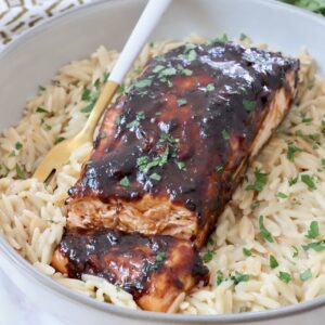 balsamic glazed salmon in a bowl with cooked orzo and a fork