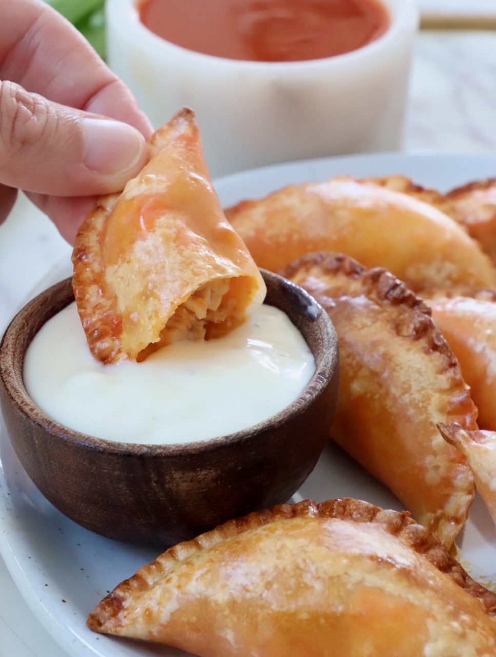 hand dipping a buffalo chicken bite in a small bowl of blue cheese dressing