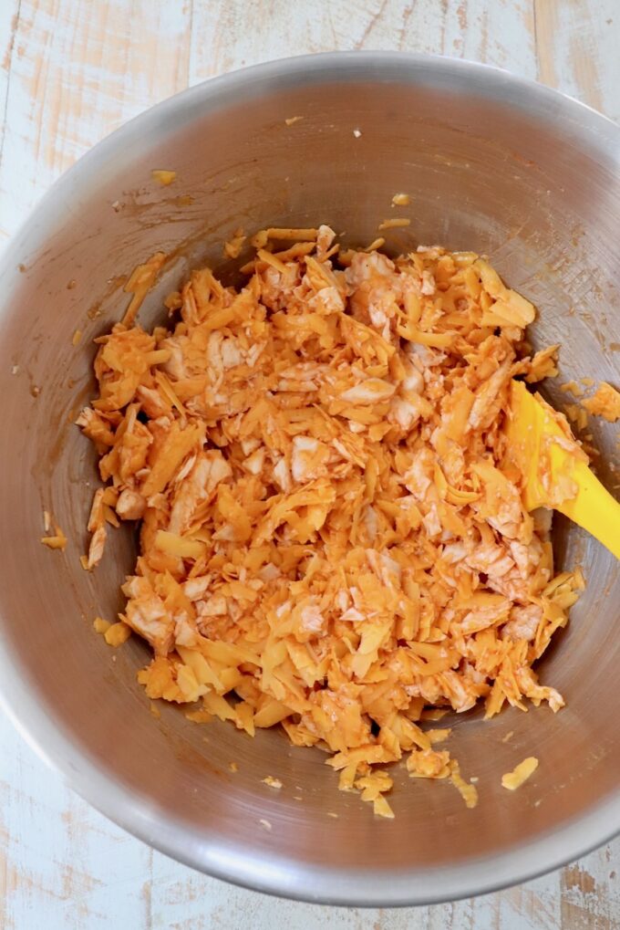 shredded chicken tossed with buffalo sauce in a bowl with a spatula