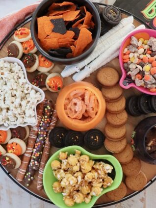 pretzels, popcorn, candies and cookies in small bowls on a wood board