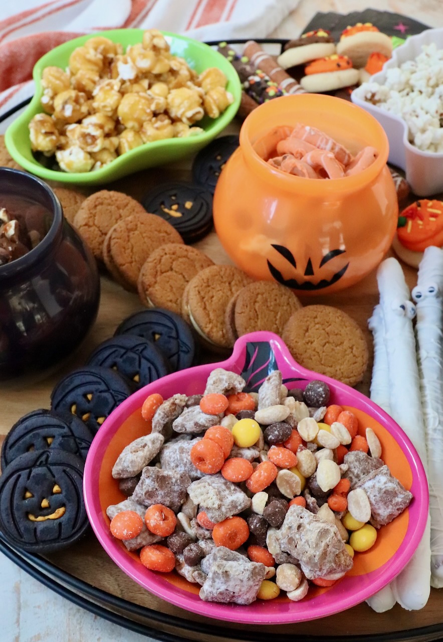 snacks in bowls on a board with cookies and pretzel rods