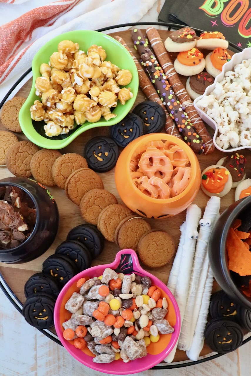 snack board with Halloween themed bowls of pretzels, candies and popcorn