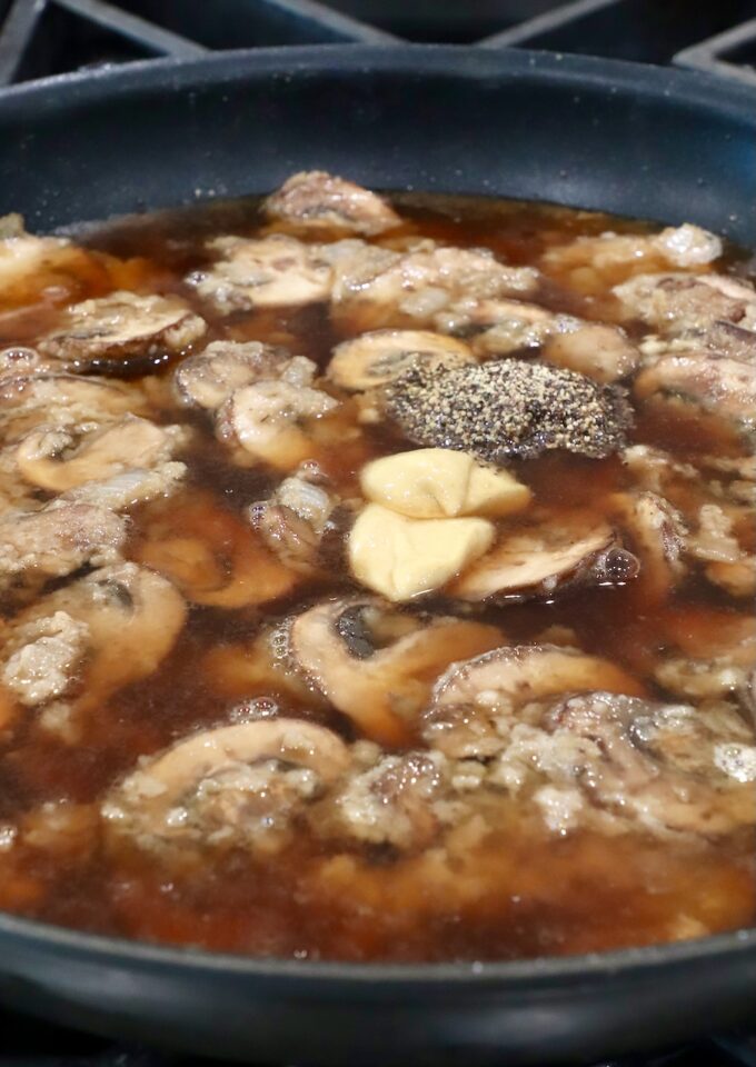 sliced mushrooms in beef broth in a skillet with dijon mustard and black pepper on top