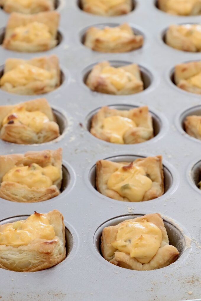 baked puff pastry dough in a mini muffin tin filled with a cream cheese filling