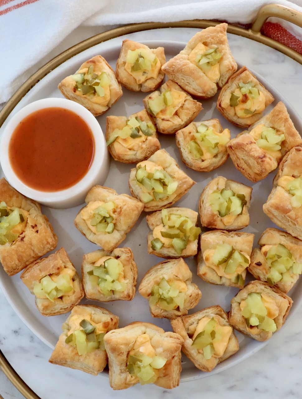 pickle puff pastry bites on a marble board with a small bowl of hot sauce