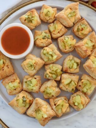 puff pastry pickles bites on a plate with a small bowl of hot sauce