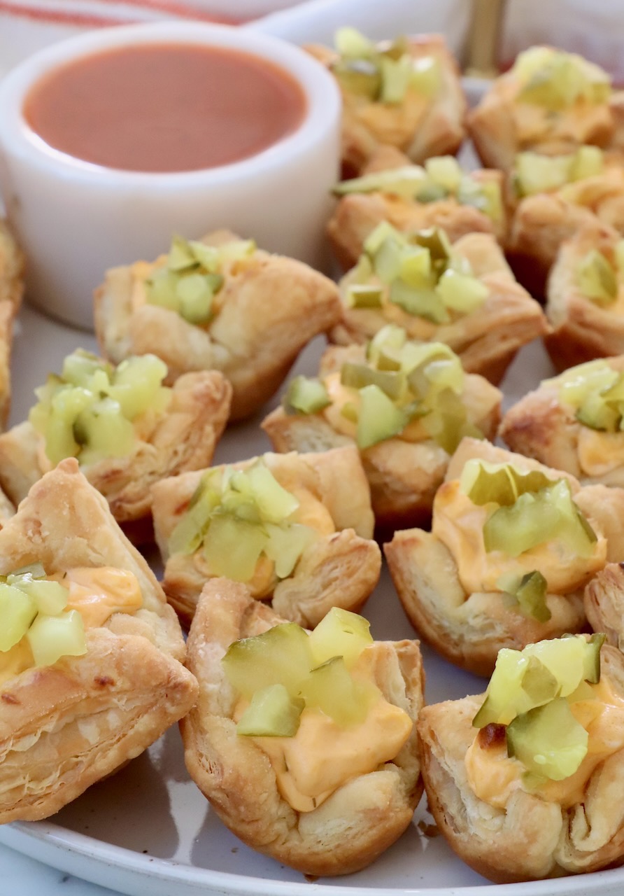 pickle puff pastry bites on a plate with a small bowl of buffalo sauce