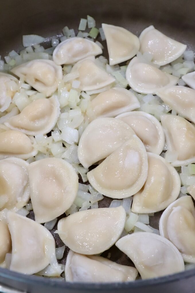 mini pierogis in a large pot with diced onions