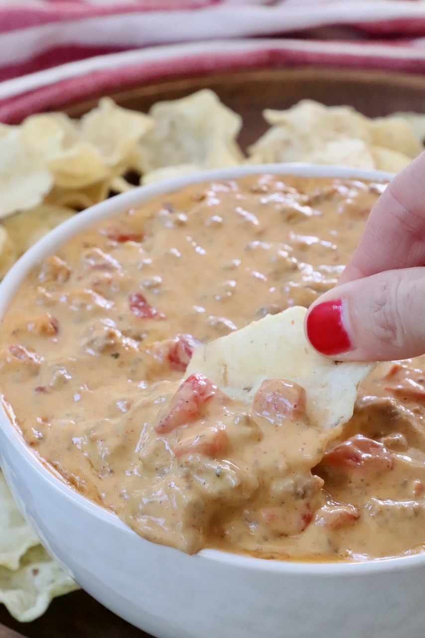 hand dipping a tortilla chip into rotel dip in a bowl