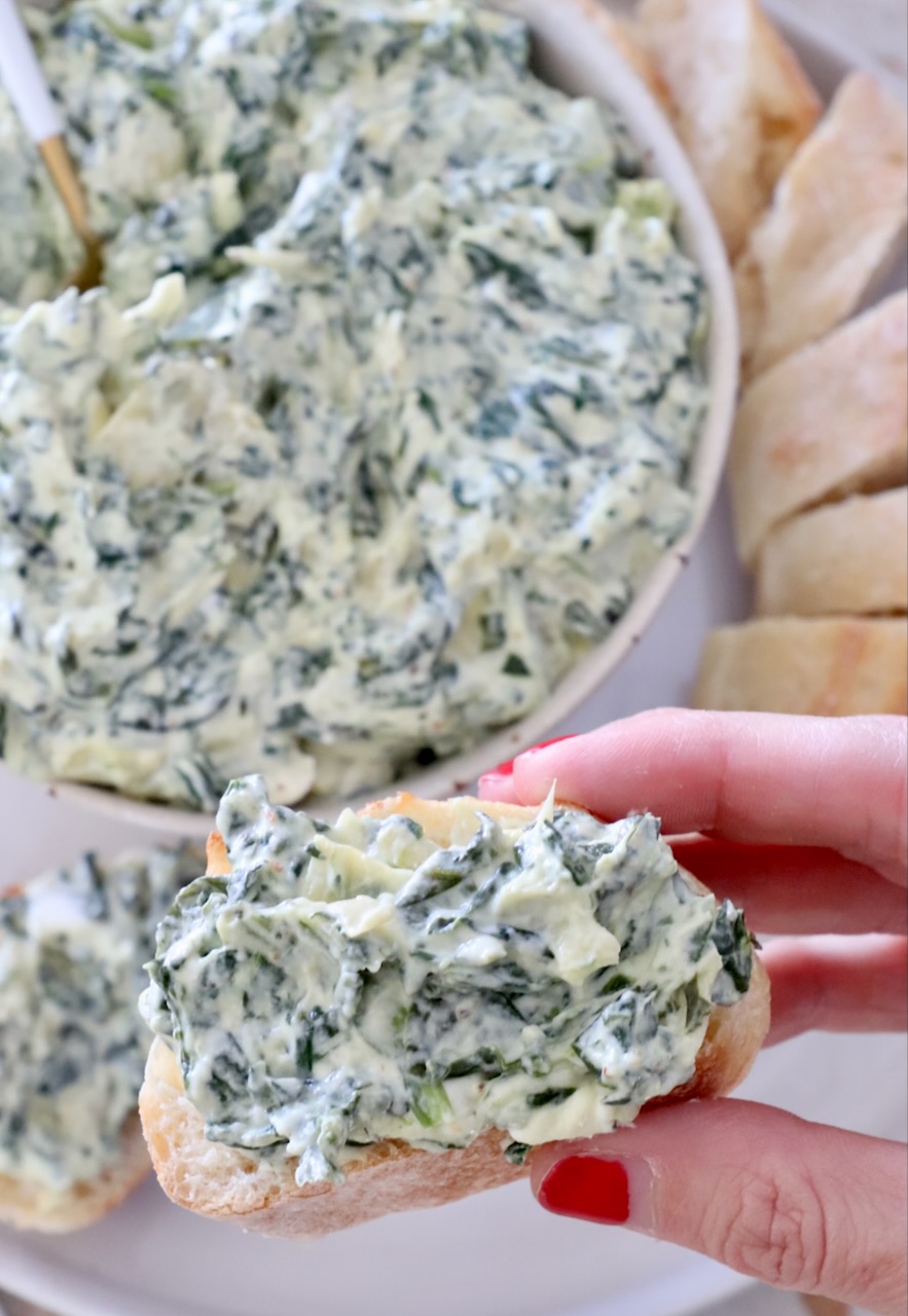 spinach artichoke dip in a bowl and spread on a slice of baguette