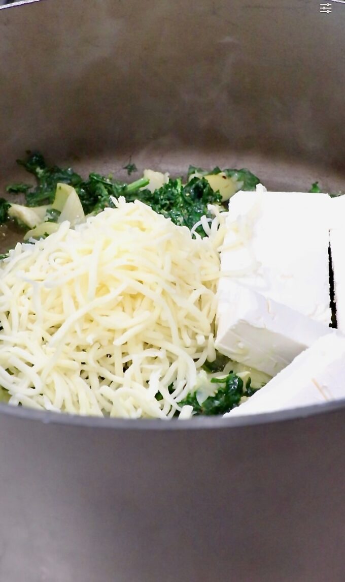 shredded mozzarella cheese and cubed cream cheese in a large pot with spinach