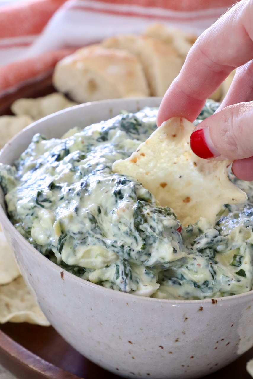 hand dipping a tortilla chip into a bowl of spinach artichoke dip