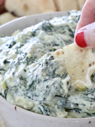 hand dipping a tortilla chip in a bowl of spinach artichoke dip