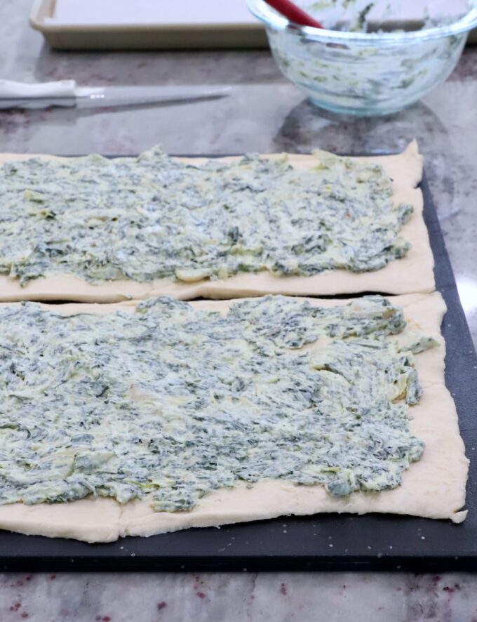 spinach artichoke dip spread on crescent roll dough on a cutting board