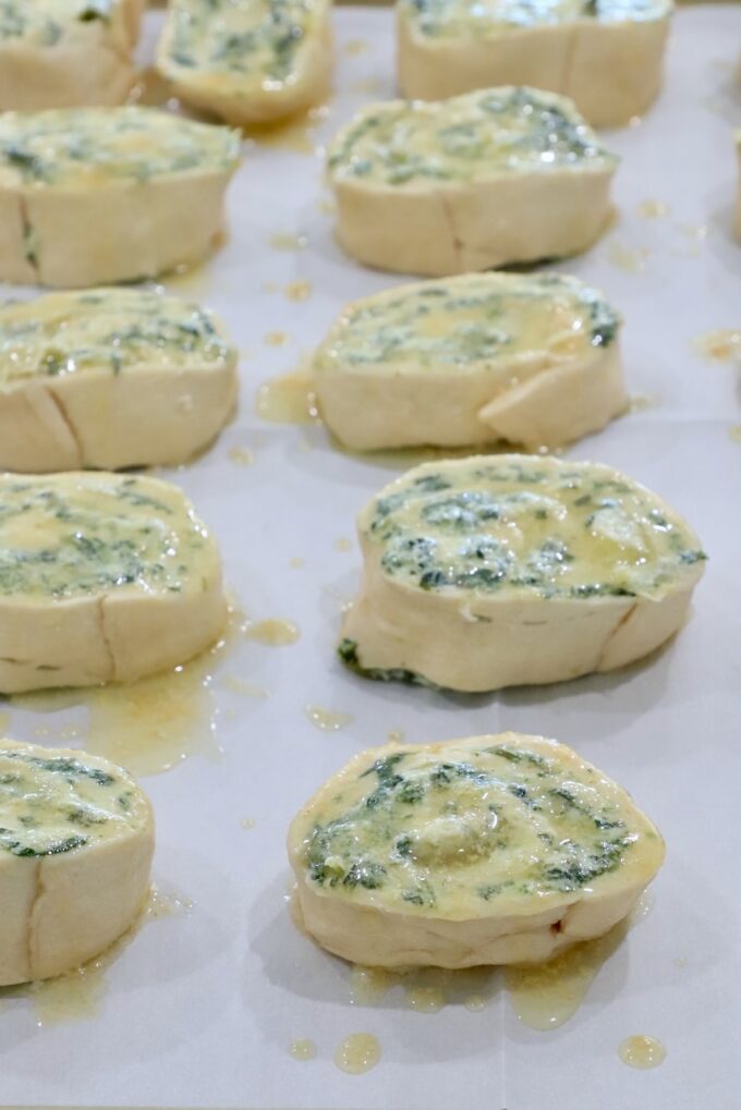 spinach artichoke rolls brushed with butter on a baking sheet