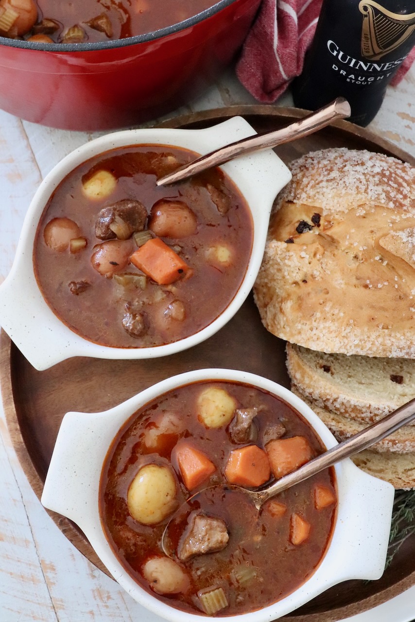 Irish stew in two bowls with spoons next to sliced bread