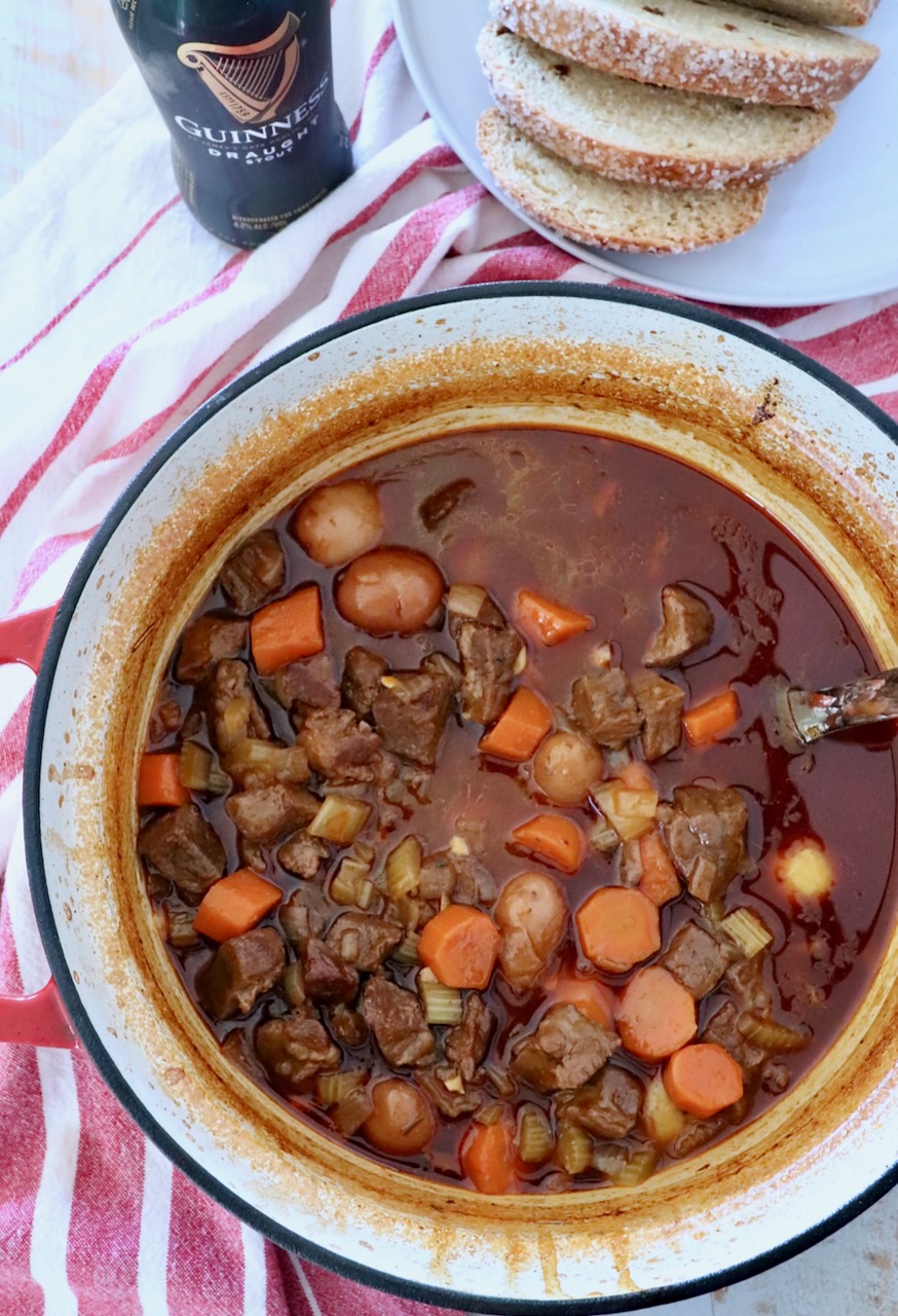 beef stew in a large cast iron pot next to a bottle of Guinness and sliced bread