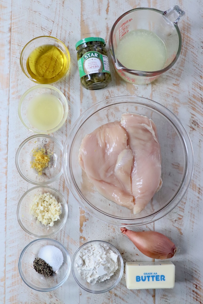 ingredients for chicken piccata on a white wood board