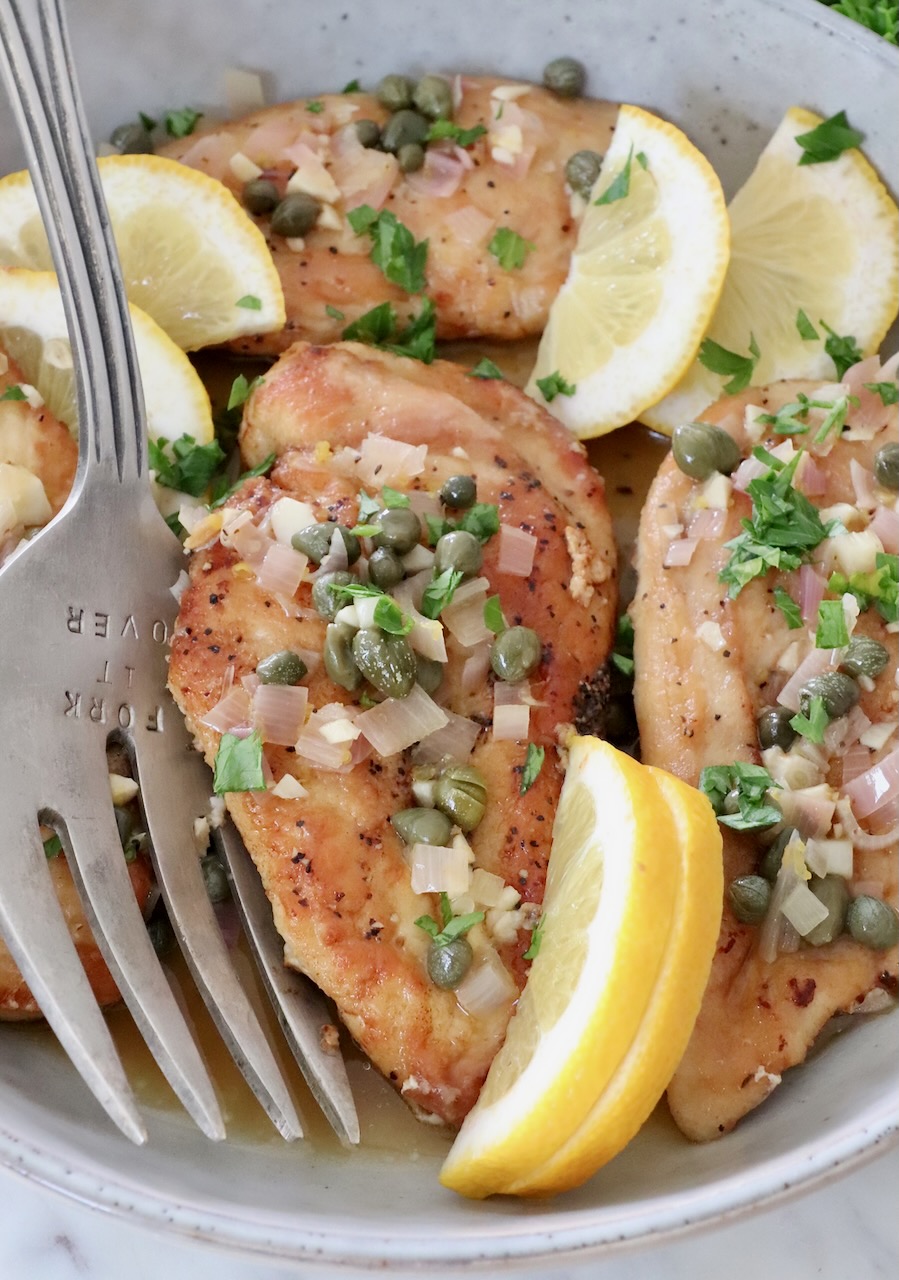 chicken piccata in a bowl with lemon wedges and a serving fork