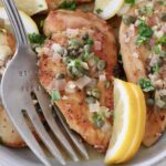 chicken piccata in a bowl with lemon wedges and a large serving fork