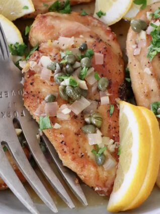 chicken piccata in a bowl with lemon wedges and a large serving fork