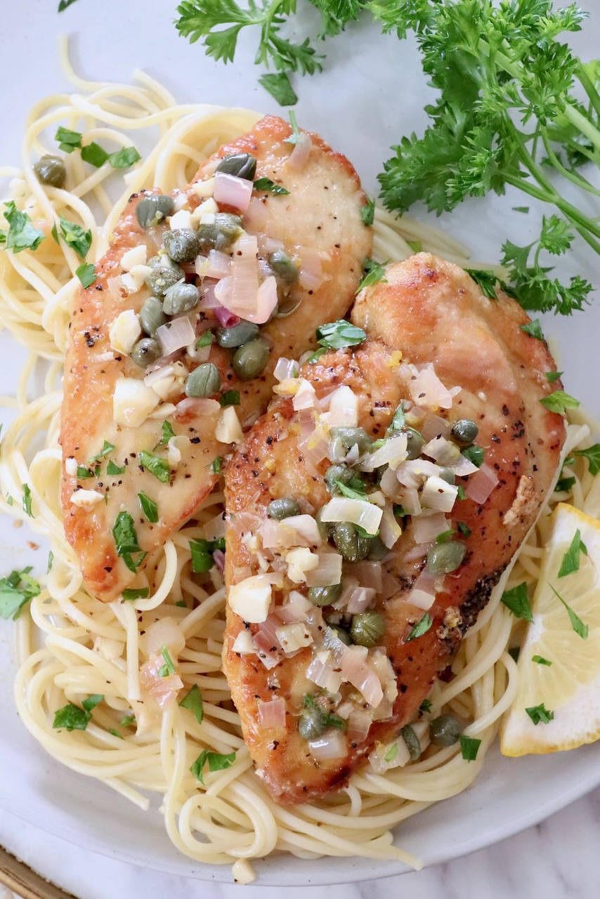 chicken piccata on top of spaghetti noodles in a bowl