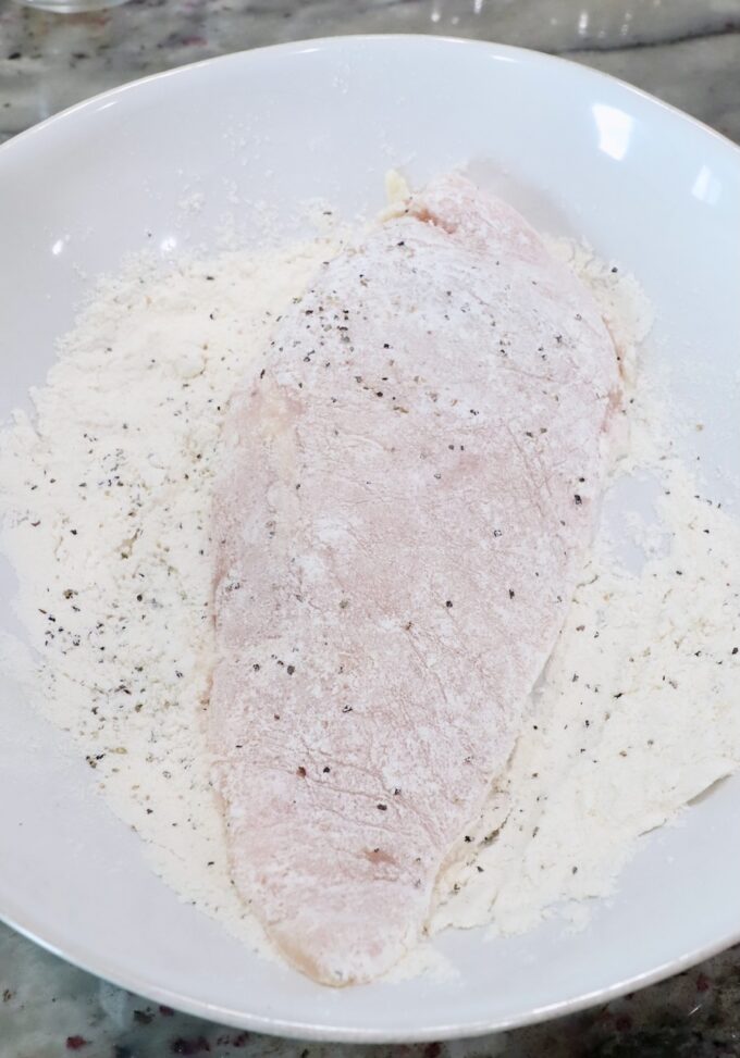 chicken breast covered in seasoned flour in a bowl