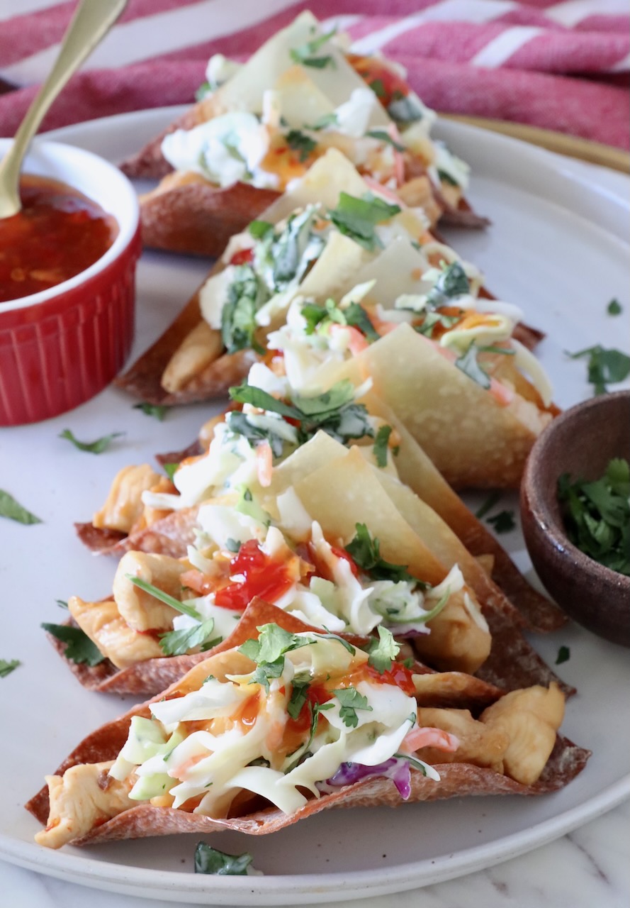 wonton tacos filled with chicken and coleslaw on a plate next to a bowl of sweet chili sauce