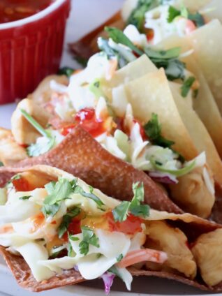 wonton taco shells filled with cooked chicken and coleslaw on a plate