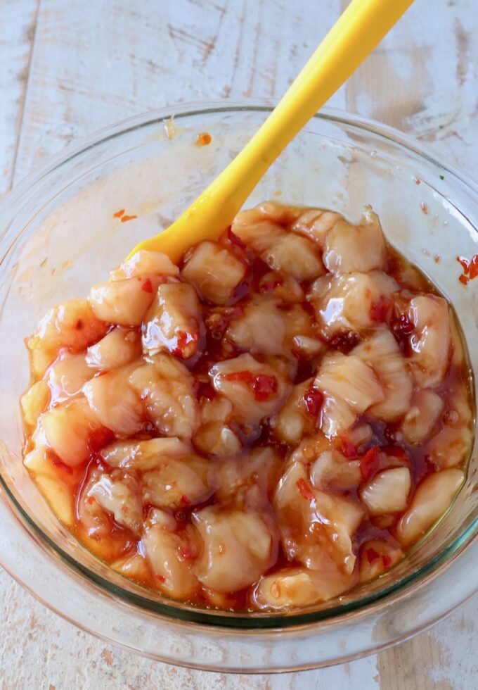 diced chicken mixed with sweet chili sauce in a glass bowl with a yellow spatula