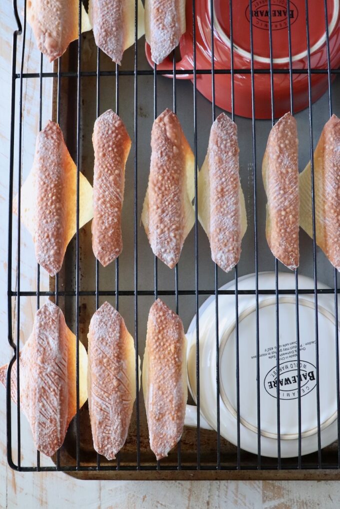 baked wonton wrappers folder over a wire rack, on top of two bowls on a baking sheet