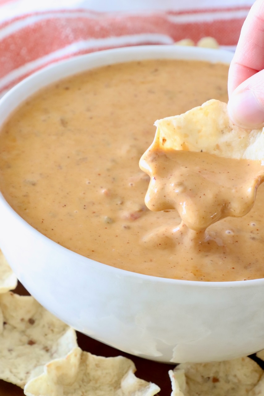 hand dipping a tortilla chip in a bowl of chili cheese dip