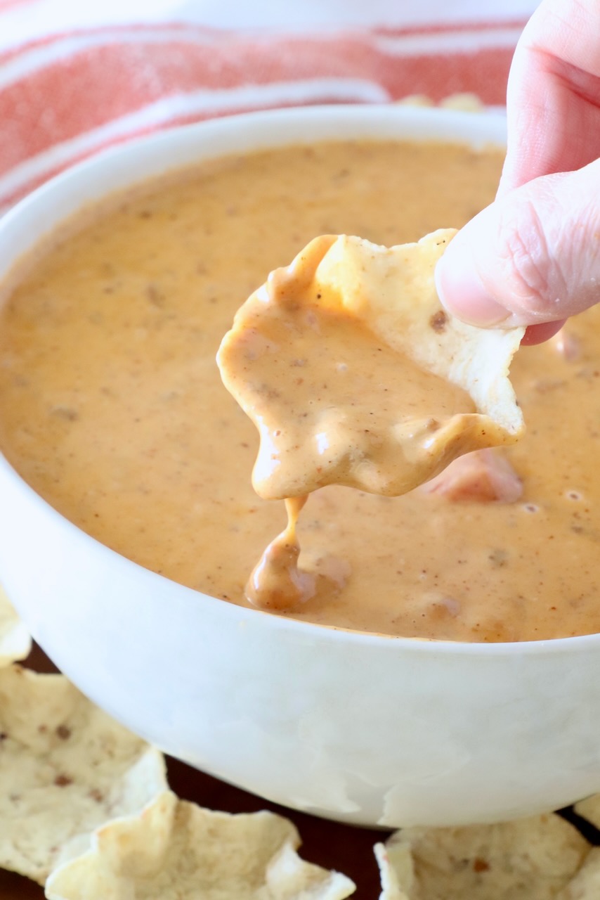 hand dipping a chip into prepared chili cheese dip in a bowl