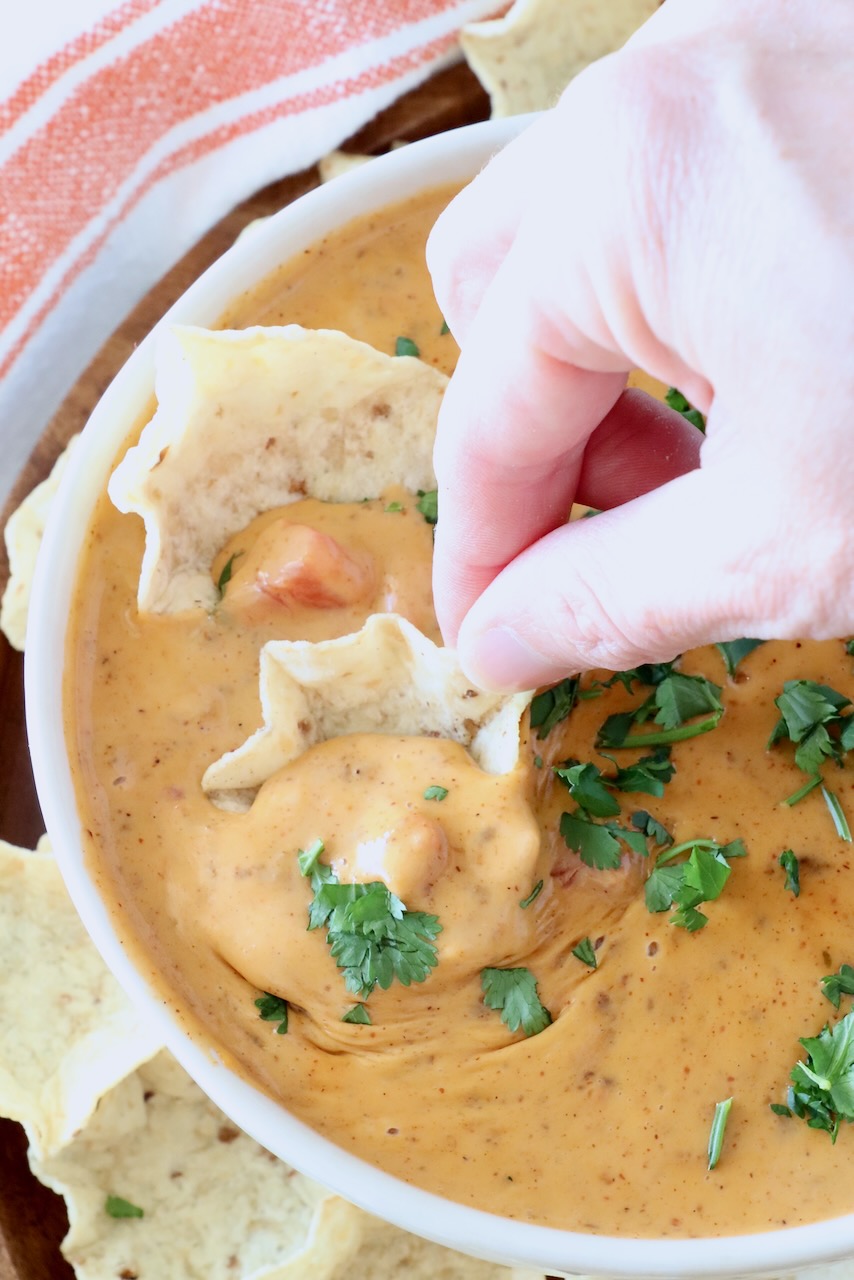 hand dipping a chip in a bowl of chili cheese dip