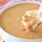 hand dipping a tortilla chip into chili cheese dip in a bowl