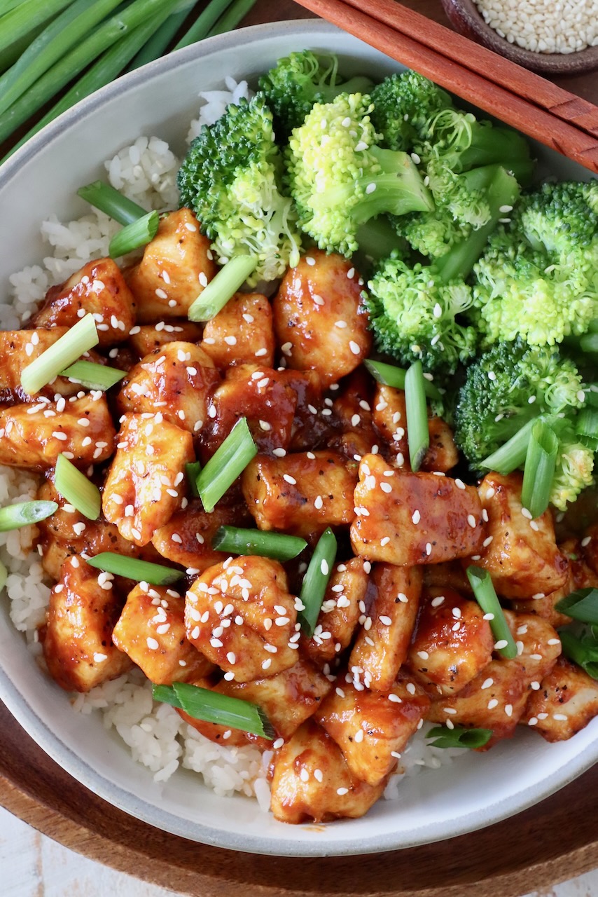 gochujang chicken in a bowl with rice, steamed broccoli and chopsticks on the side