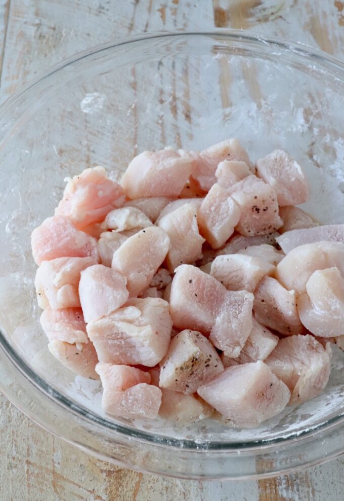 pieces of chicken tossed in seasoned cornstarch in a glass bowl