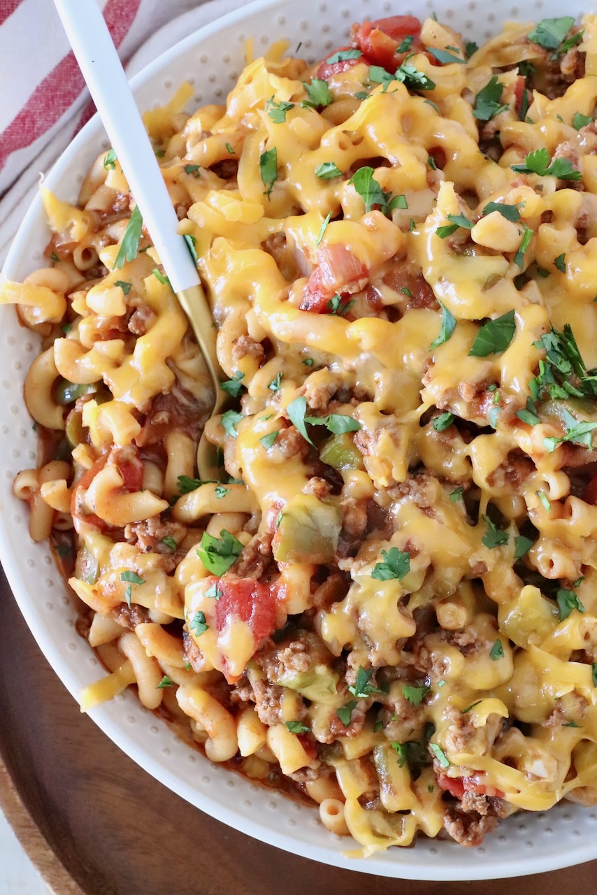 prepared goulash in a bowl with a spoon, covered with shredded cheddar cheese