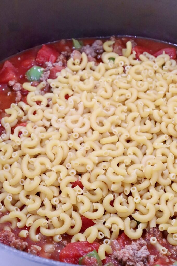 uncooked macaroni noodles in a pot with tomato sauce