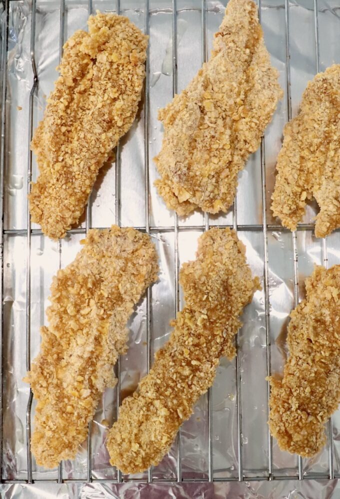 breaded chicken strips on a wire rack on top of a baking sheet